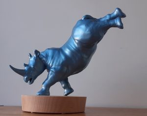 a sculpture of a blue rhinoceros dancing, set on a wooden base