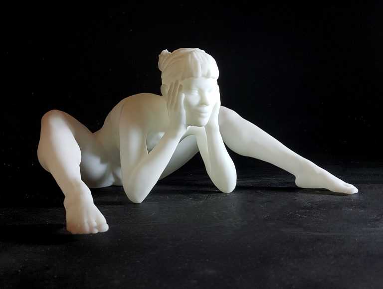 A white figurine of a nude woman siiting and leaning forward