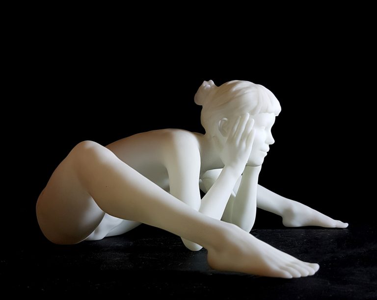 A white figurine of a nude woman siiting and leaning forward