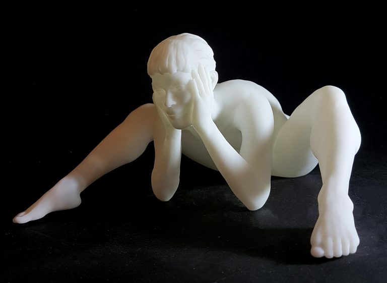 A white figurine of a nude woman siiting and leaning forward