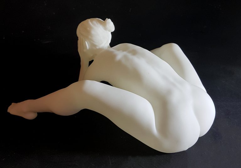 A white figurine of a nude woman siiting and leaning forward